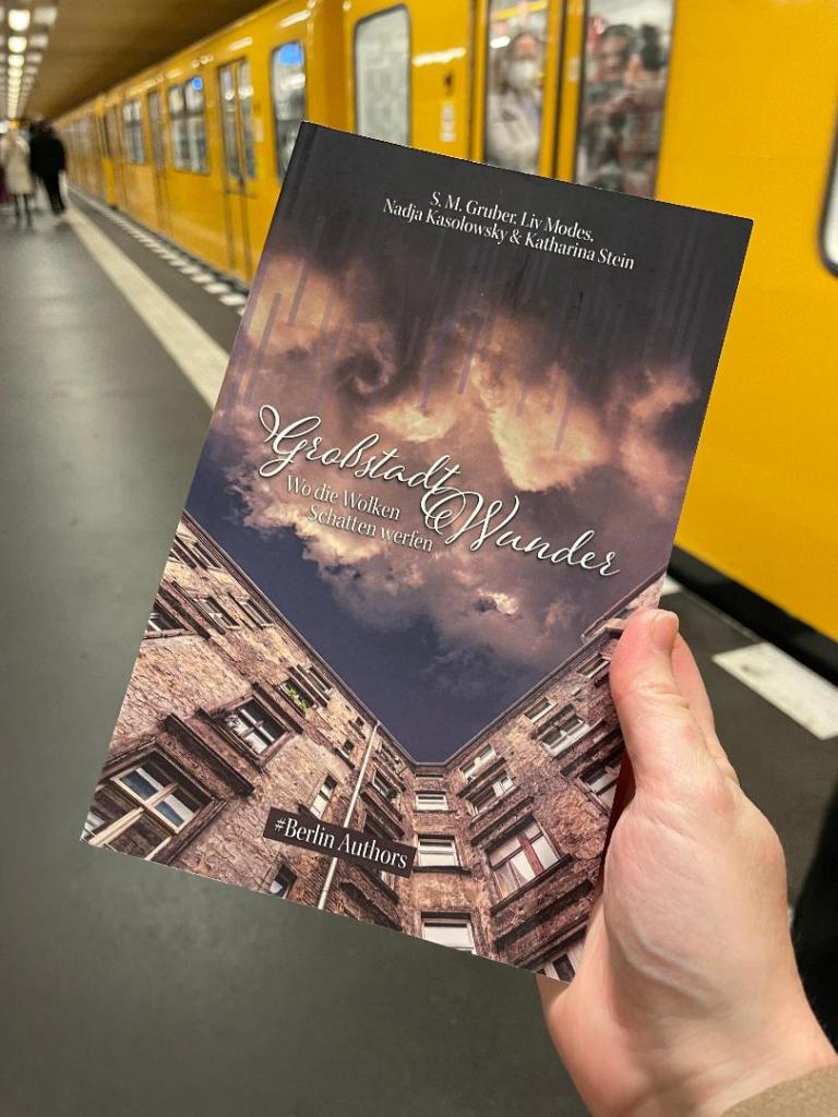 Großstadtwunder Anthologie (2022) Kurzgeschichtenband/Cover der #BerlinAuthors, gehalten in Berliner U-Bahn, U-Bahn im Hintergrund.